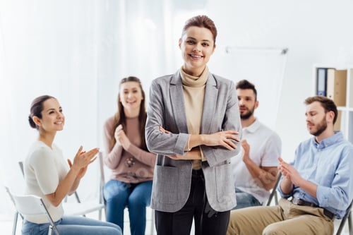 Preview: smiling woman looking at camera while people sitting and applauding during group therapy session