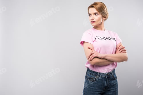 Preview: woman in pink feminist t-shirt posing with crossed arms, isolated on grey
