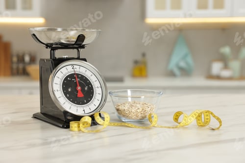 Preview: Kitchen scales, oatmeal in bowl and measuring tape on light marble table indoors