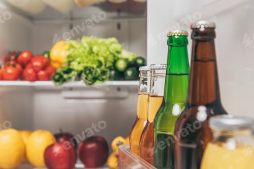 Preview: selective focus of bottles of beer on fridge door near fresh food on shelves