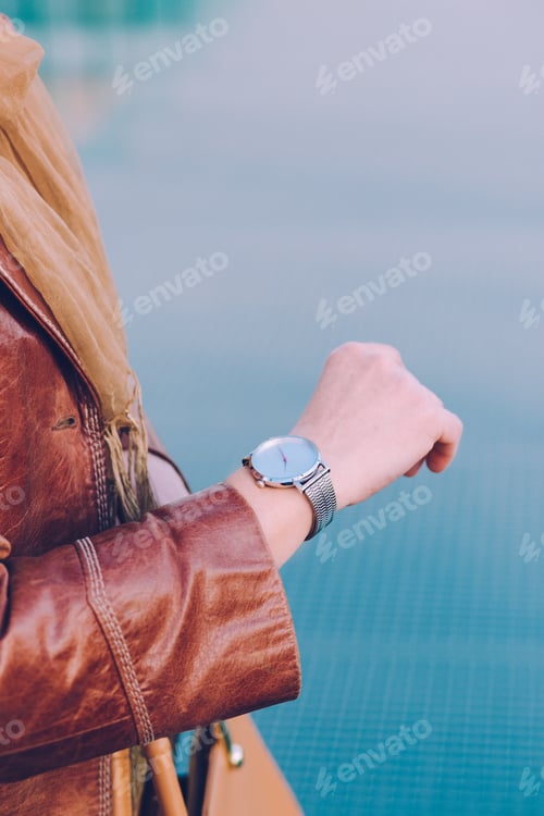 Preview: Elegant woman wearing silver wristwatch and brown leather coat holding leather brown handbag