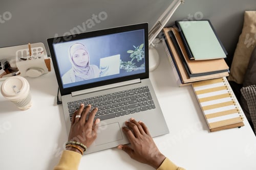 Preview: Laptop on desk with teacher in hijab on the screen during online lesson