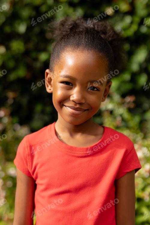 Preview: Portrait of cute smiling african american girl standing against plants outdoors
