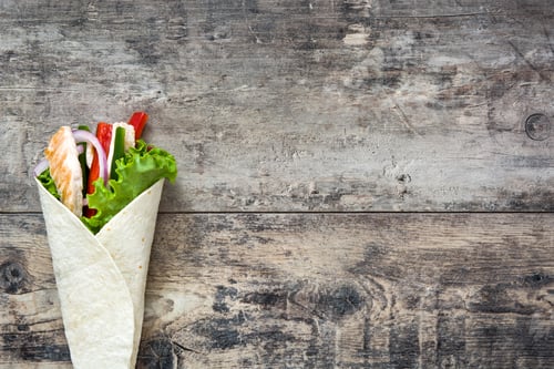 Preview: Chicken wrap with vegetables on rustic wooden table: overhead view with copy space