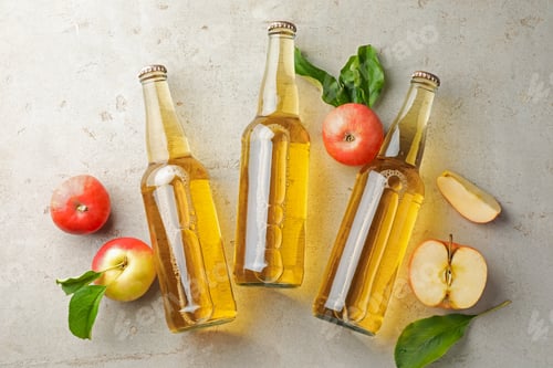 Preview: Delicious cider in glass bottles and apples on gray textured table, flat lay