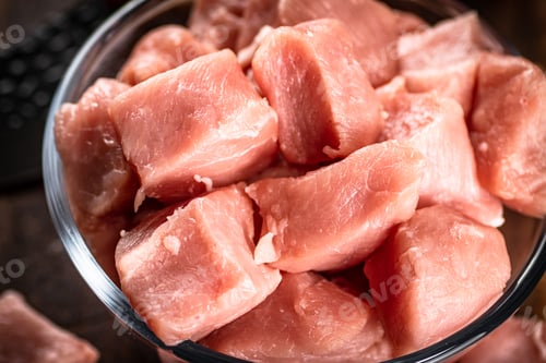 Preview: Pieces of raw pork in a bowl on a cutting board.