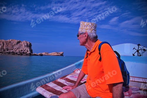 Preview: Senior tourist with Oman hat sitting on the boat and sailing along the coast