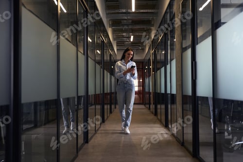 Preview: Cheerful female using her mobile phone in office hallway