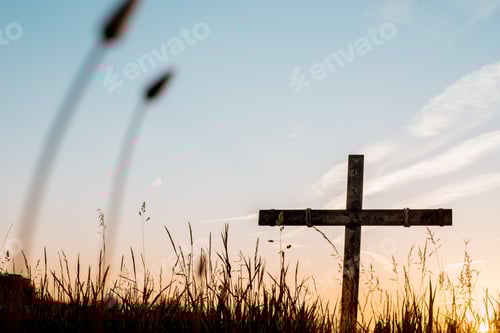 Preview: Low angle shot of a handmade wooden cross in a grassy field with a beautiful sky in the background