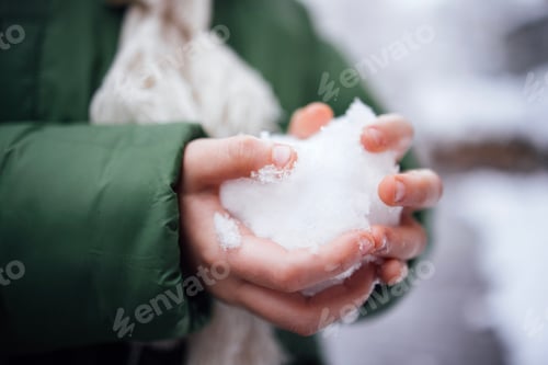 Preview: Person holding a snowball in hands, wearing a green winter jacket and a light scarf