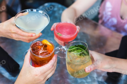 Preview: Four hands clinking colorful cocktails at a restaurant sitting at a patio outside