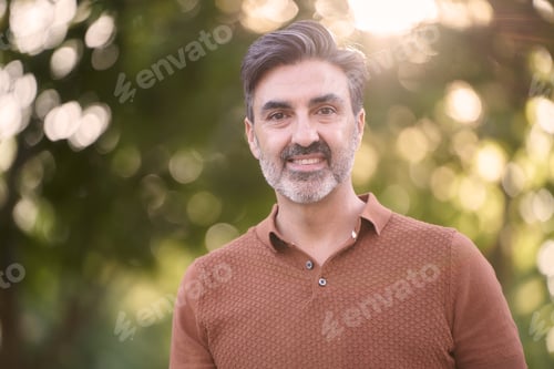 Preview: Relaxed middle-aged man looking at camera while standing outdoors in a park.