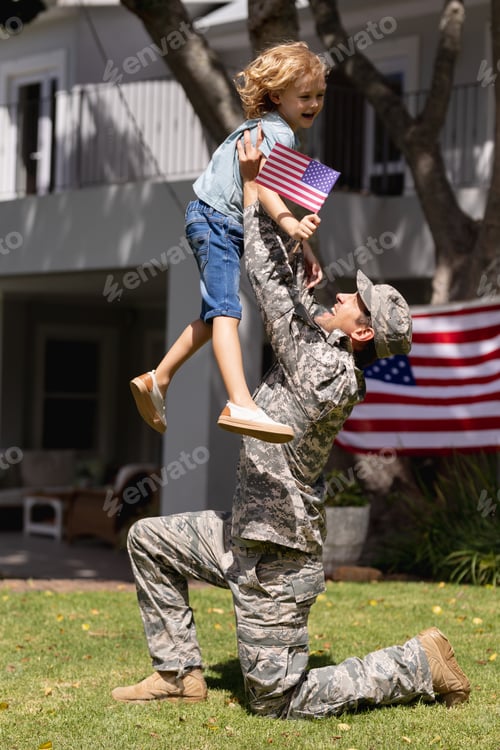 Preview: Smiling caucasian soldier father lifting happy son in garden with american flag outside house