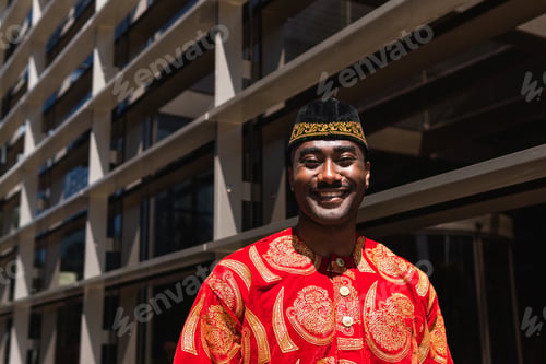 Preview: Smiling African man in traditional clothes and headdress near building
