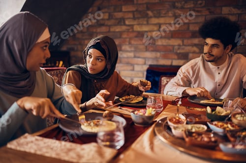 Preview: Young Arabian woman talking to her friends during a meal at dining table on Ramadan.