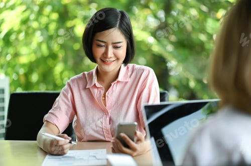 Preview: New businesswoman sitting in office using a mobile phone and smiling.