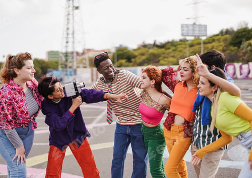 Preview: Group of multiracial young people having fun together outdoor while using vintage video camera