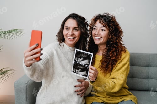 Preview: LGBT lesbian couple holding ultrasound photo scan on video call of growing baby in pregnancy time