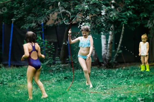 Preview: Three children sisters splashing water from a hose in the backyard, in the garden
