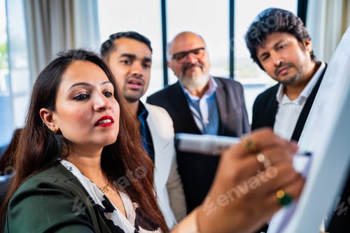 Preview: Indian Asian Corporate team discussing a strategy drawn on whiteboard by a young businesswoman