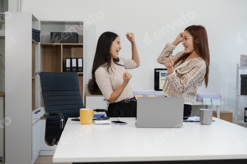 Preview: Excited businesswomen celebrating success, teamwork, and achievement in a modern office.
