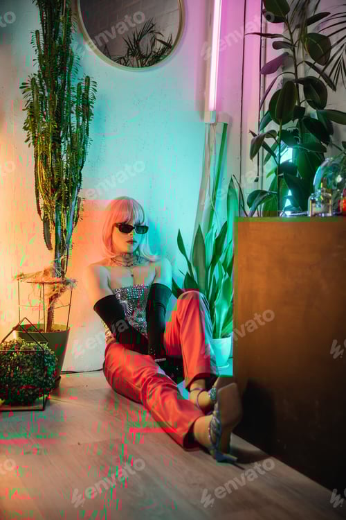 Preview: Stylish transgender person in sunglasses sitting on floor near plants at home