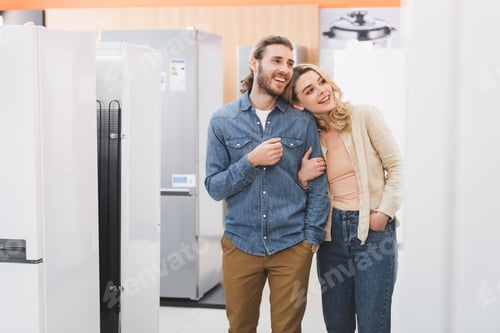Preview: smiling boyfriend and girlfriend looking at fridge in home appliance store
