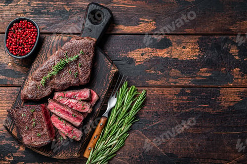 Preview: Grilled sliced skirt beef meat steak on a cutting board with herbs. Dark wooden background.