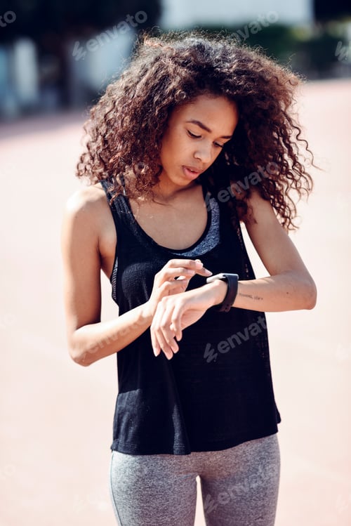 Preview: Sporty young woman looking at her smartwatch outdoors