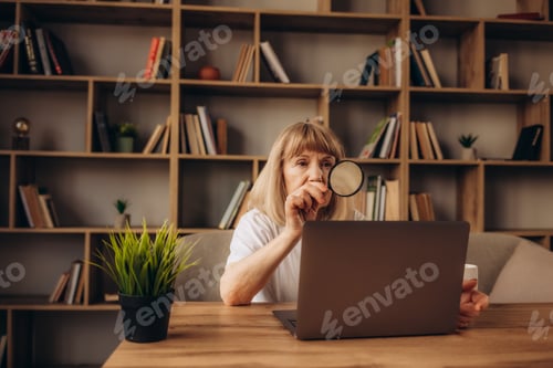 Preview: Elderly woman grandmother learns to work at home on laptop computer and internet with magnifier.