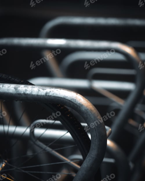 Preview: Close-up of weathered metal bike racks with curved bars, on a dark blur background