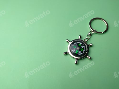 Preview: Top view of a compass keychain on a green background with copy space and text
