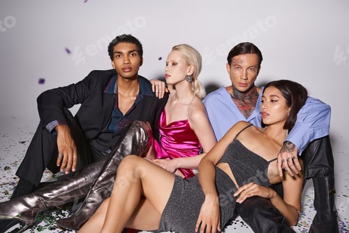 Preview: group of four interracial friends in festive attire sitting on shiny confetti after Christmas party