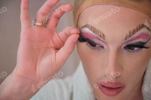 Preview: Drag queen person removing false eyelashes and wearing bathrobe.