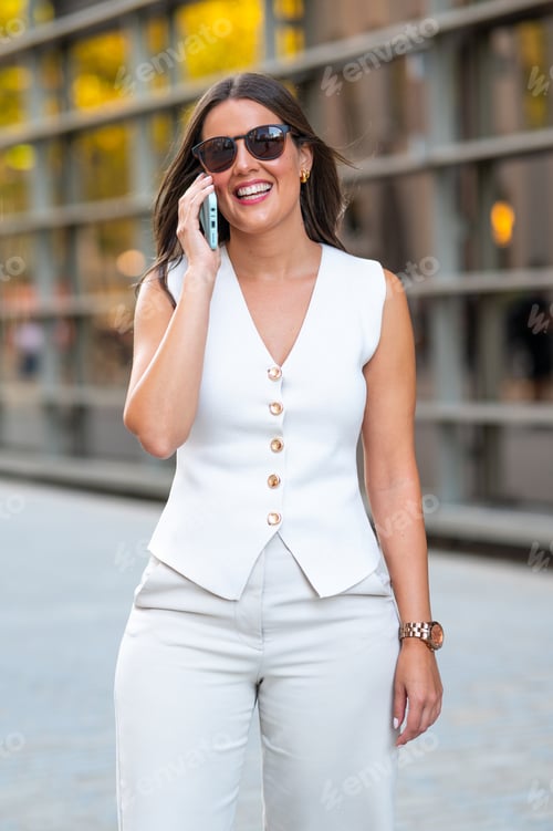 Preview: Smiling businesswoman walking and talking on phone in the city