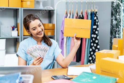 Preview: Young Asian woman holding US dollars lot of money with box,she is happy and proud smile work at home