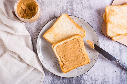 Preview: Peanut butter sandwich on toasted bread on a plate and jar of butter on the table. Top view
