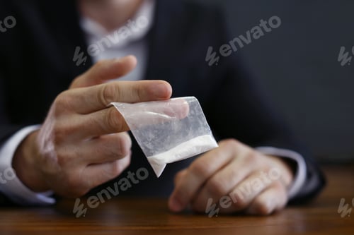 Preview: Criminal holding drug at table indoors, closeup