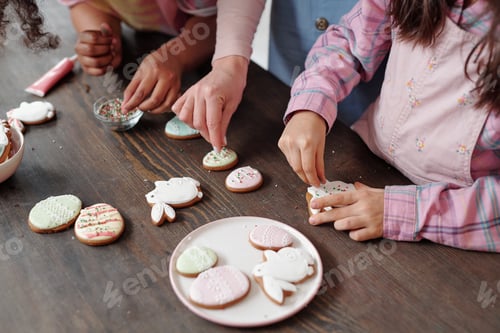 Preview: Hands of little girls and young woman decorating homemade cookies with sprinkles