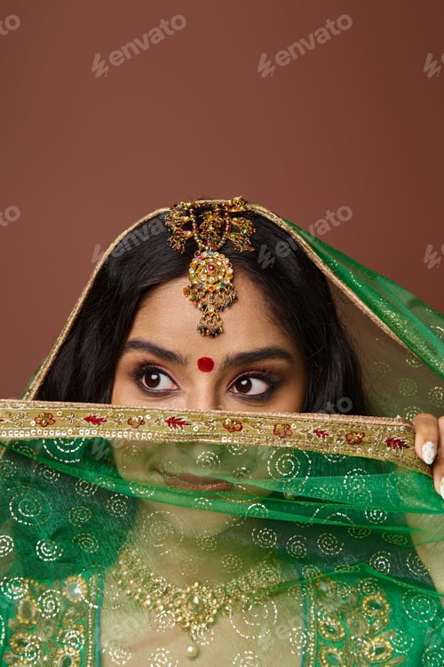Preview: vertical shot of beautiful indian woman in with bindi dot covering face with veil and looking away