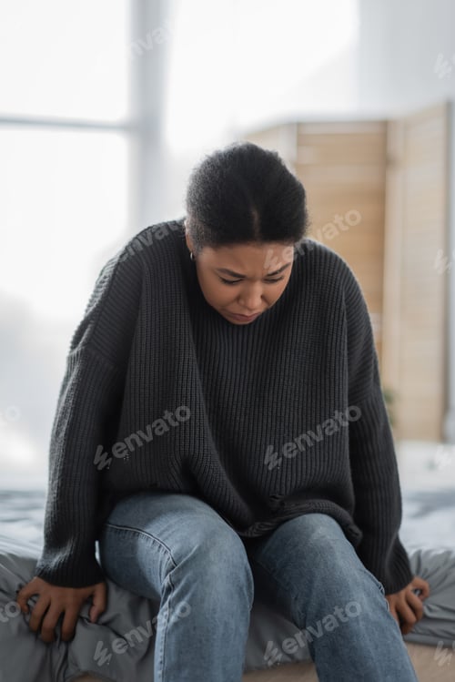 Preview: Young multiracial woman with mental problem sitting on bed at home