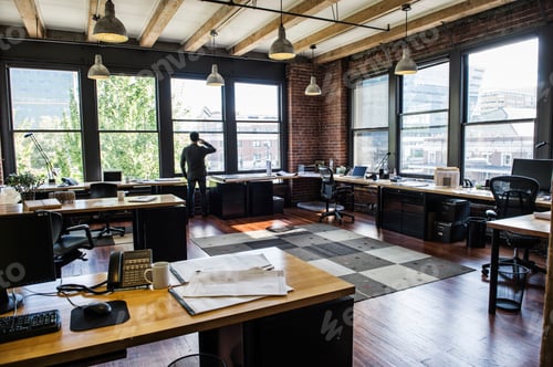 Preview: Male office worker on phone looking out windows of a creative office.