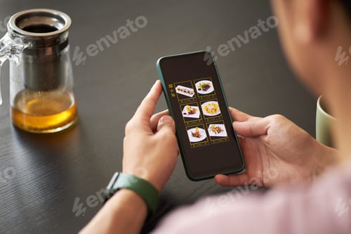 Preview: Young Adult Asian Man Ordering Food Online Using Smartphone at Table