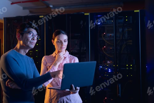 Preview: Diverse male and female engineers using laptop in computer server room