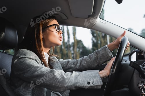 Preview: displeased businesswoman looking ahead and beeping while driving car