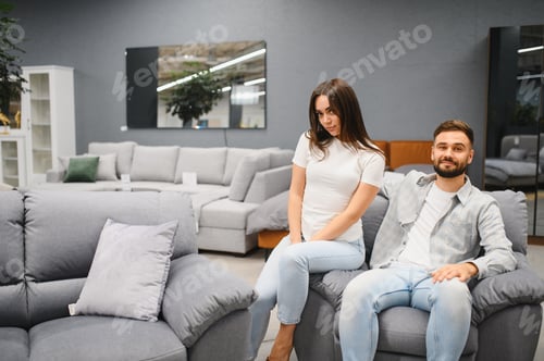 Preview: Young couple sitting on sofa in furniture store