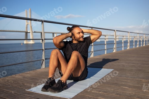 Preview: Cheerful sporty guy exercising on pier outdoors next to sea