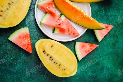 Preview: Fresh yellow and red watermelon slices arranged on a textured green surface.