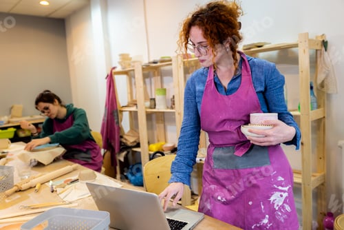 Preview: Female business owner using laptop in pottery studio workshop.