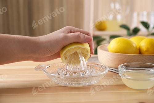 Preview: Woman squeezing lemon juice with reamer at wooden table, closeup